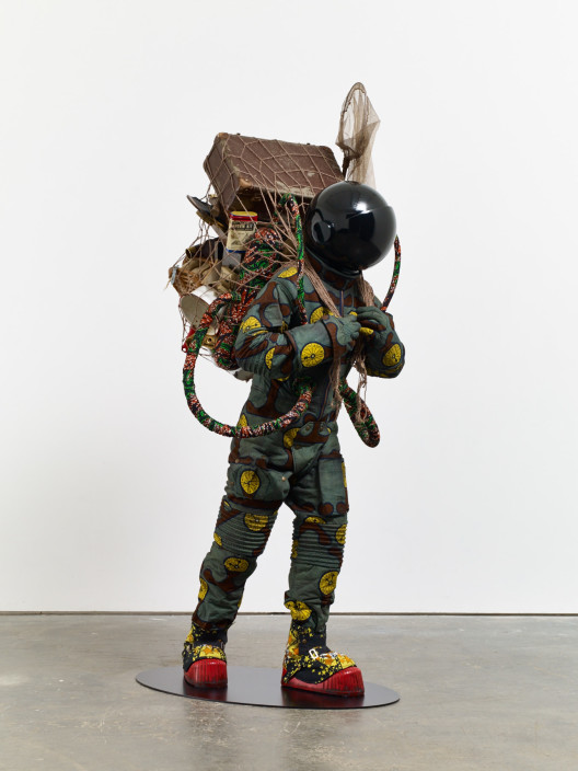 Yinka Shonibare, “Refugee Astronaut”, fibreglass mannequin, Dutch wax printed cotton textile, net, possessions, astronaut helmet, moon, boots and steel baseplate, 208 x 93 x 90 cm, 2015.